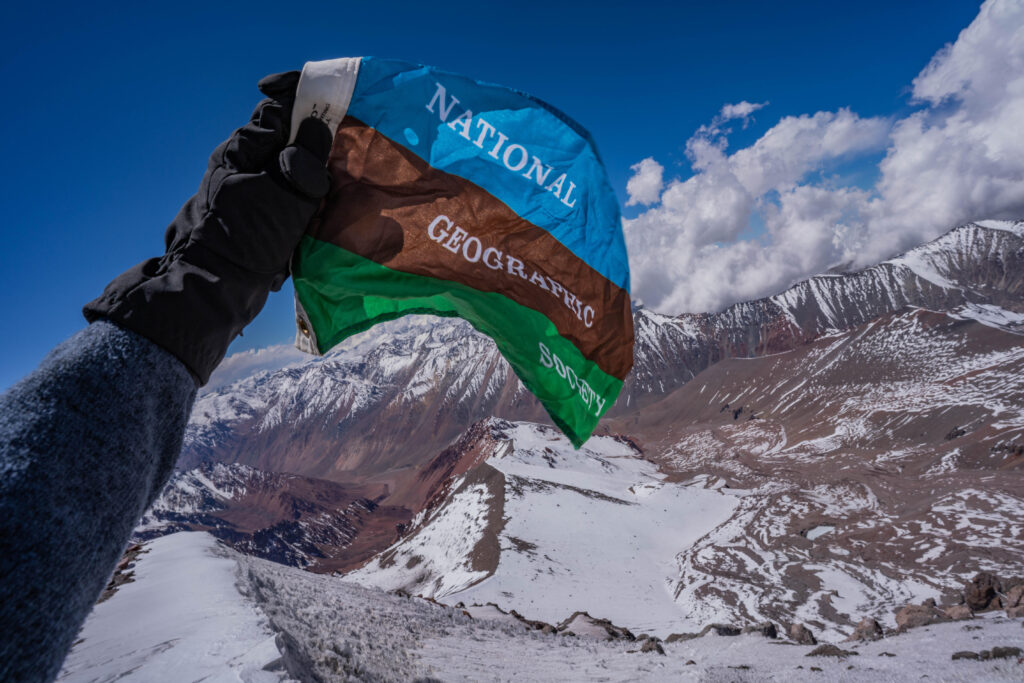 A National Geographic photographer holds the National Geographic Society flag at a mountain camp in Chile.